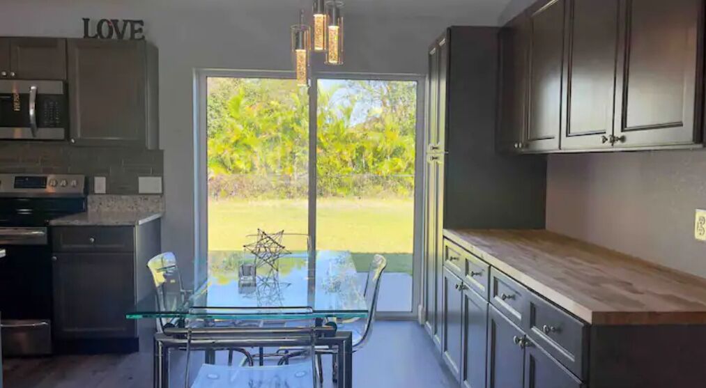 A modern kitchen with a glass dining table, dark cabinetry, and a view of a garden through glass doors.
