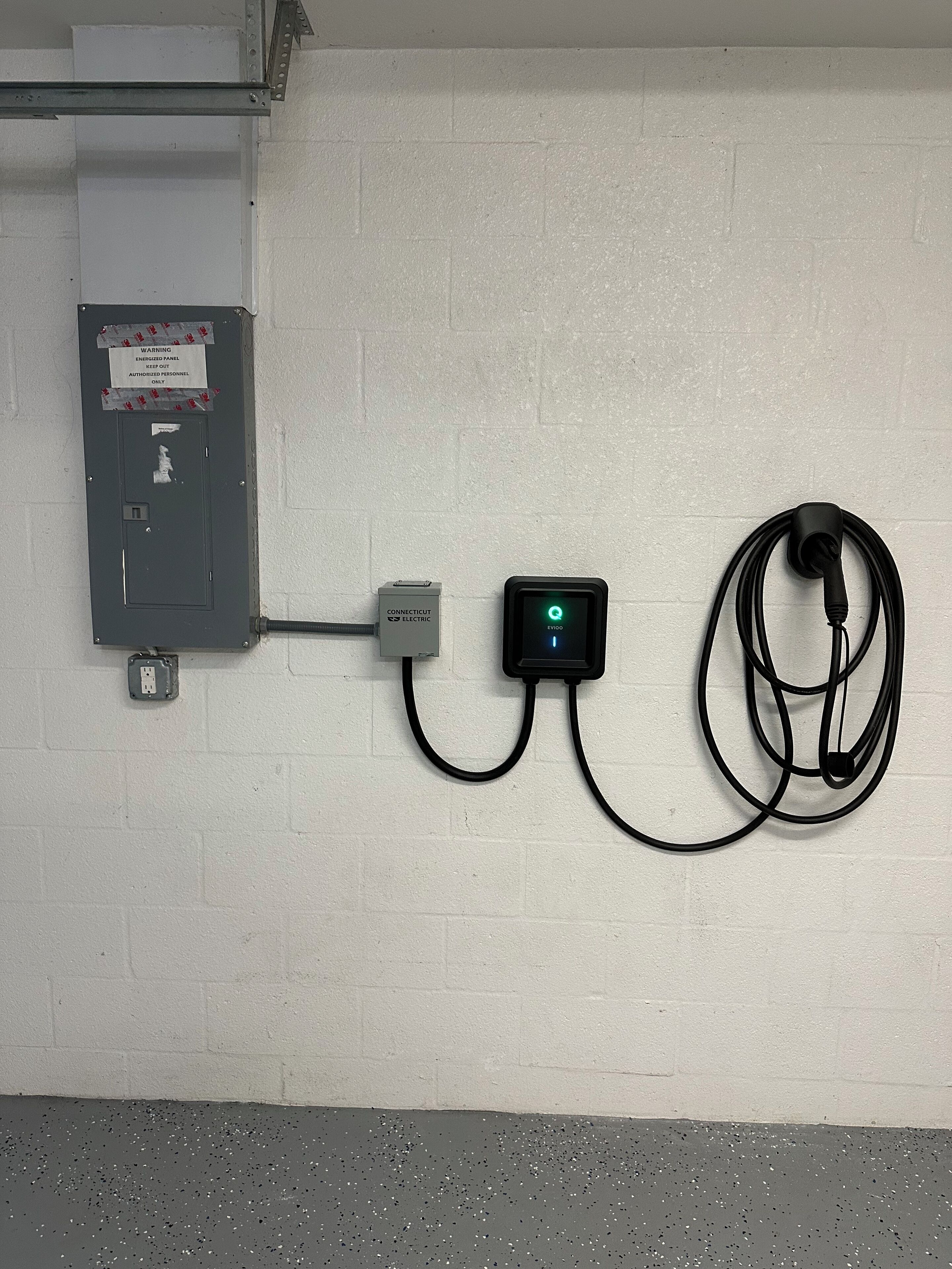 A wall-mounted electrical panel with a warning sign, a digital display, and a coiled cable.