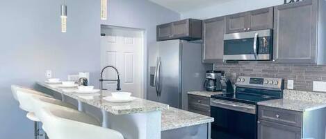A modern kitchen with stainless steel appliances, a granite countertop, and a bar area with white barstools.