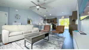 A modern living room with a white sofa, two armchairs, a wooden coffee table, and a ceiling fan.