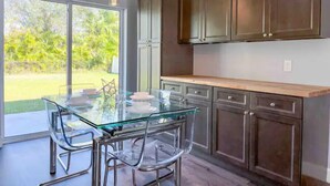 A modern kitchen with glass-top dining table and chairs, wooden cabinets, and pendant lighting.