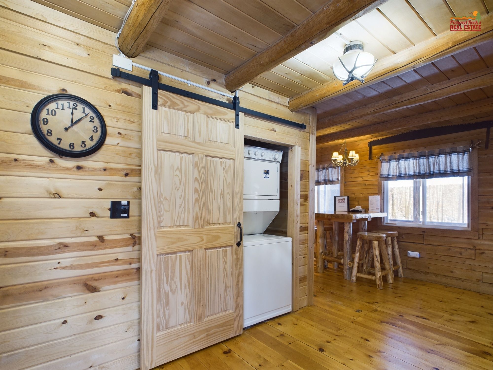 Interior de una cabaña de madera con una zona de cocina, un reloj y una puerta corrediza.