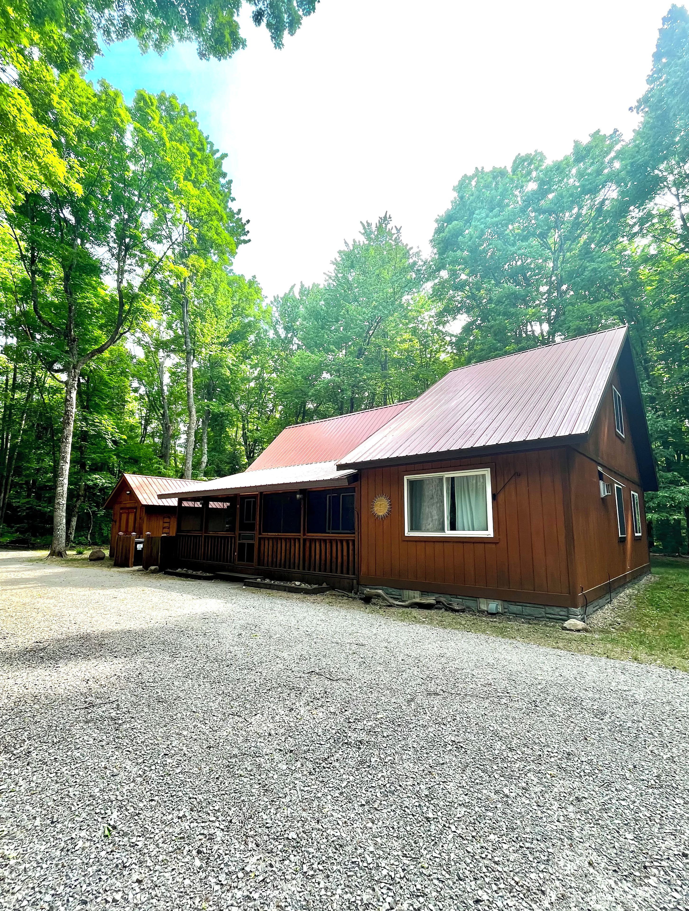 A wooden cabin with a gravel driveway, surrounded by trees.