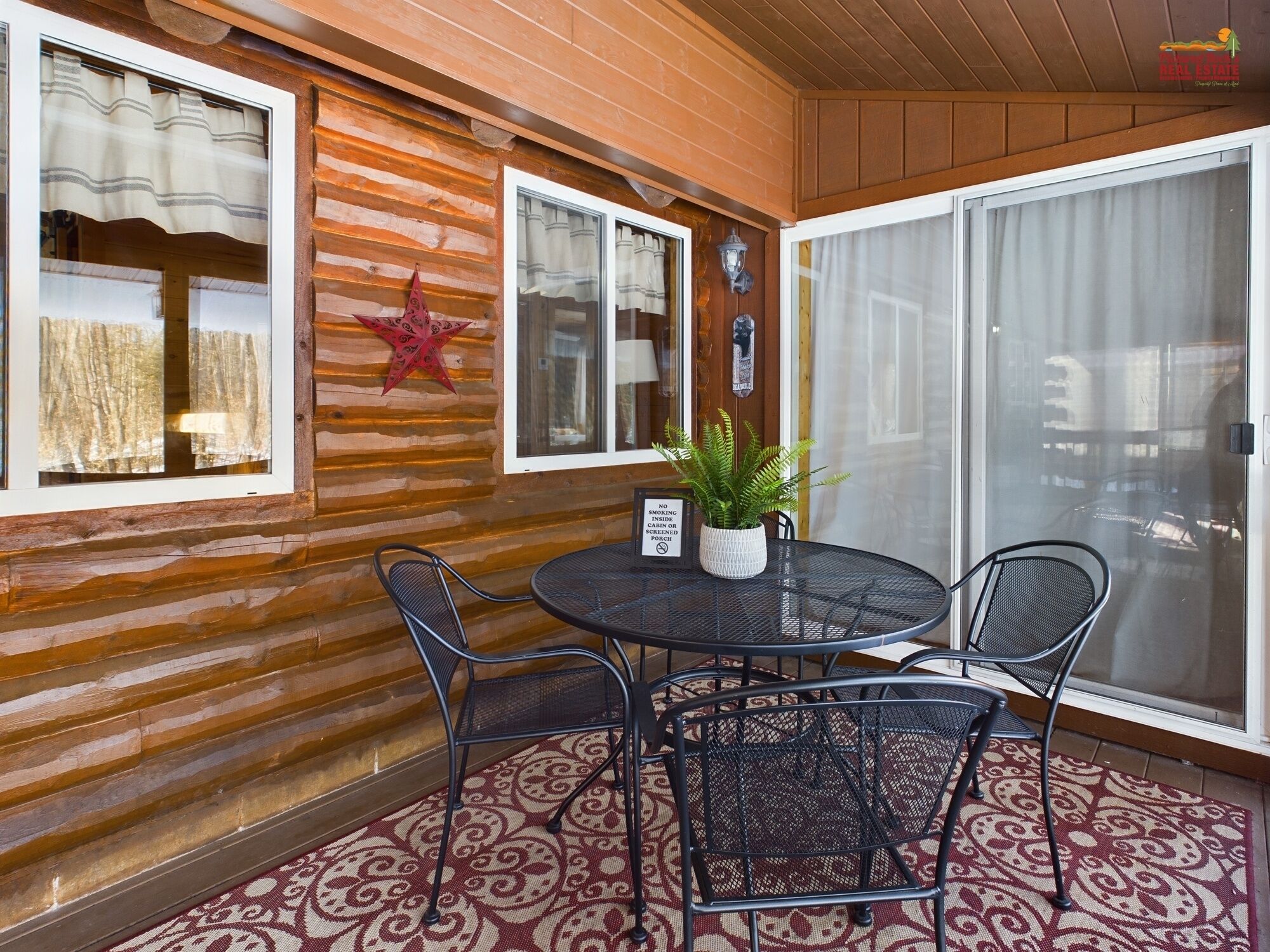 A wooden cabin with a round table and four chairs, a star decoration, and a sign prohibiting smoking inside.