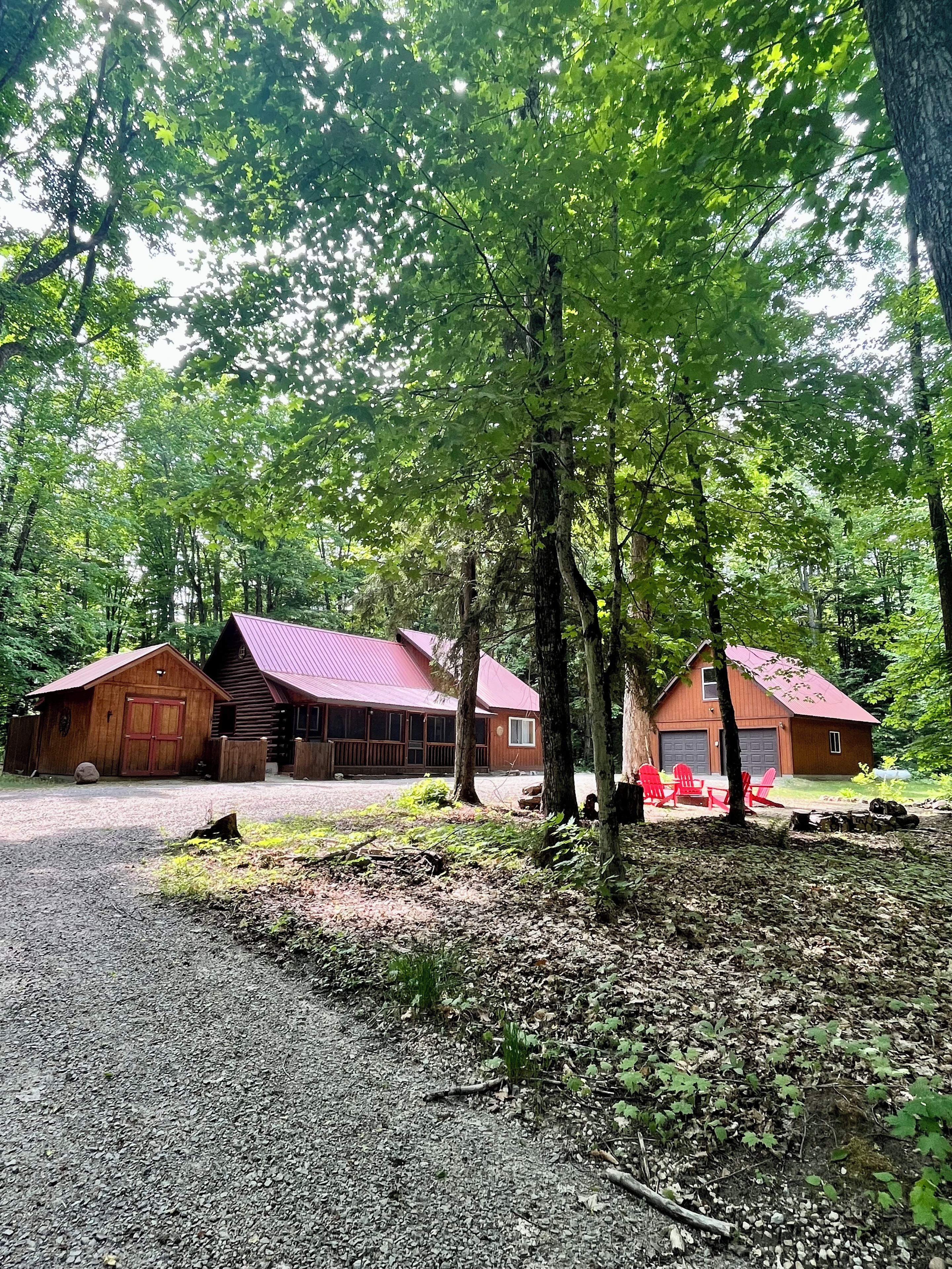 A rustic cabin with a red roof, surrounded by dense forest.