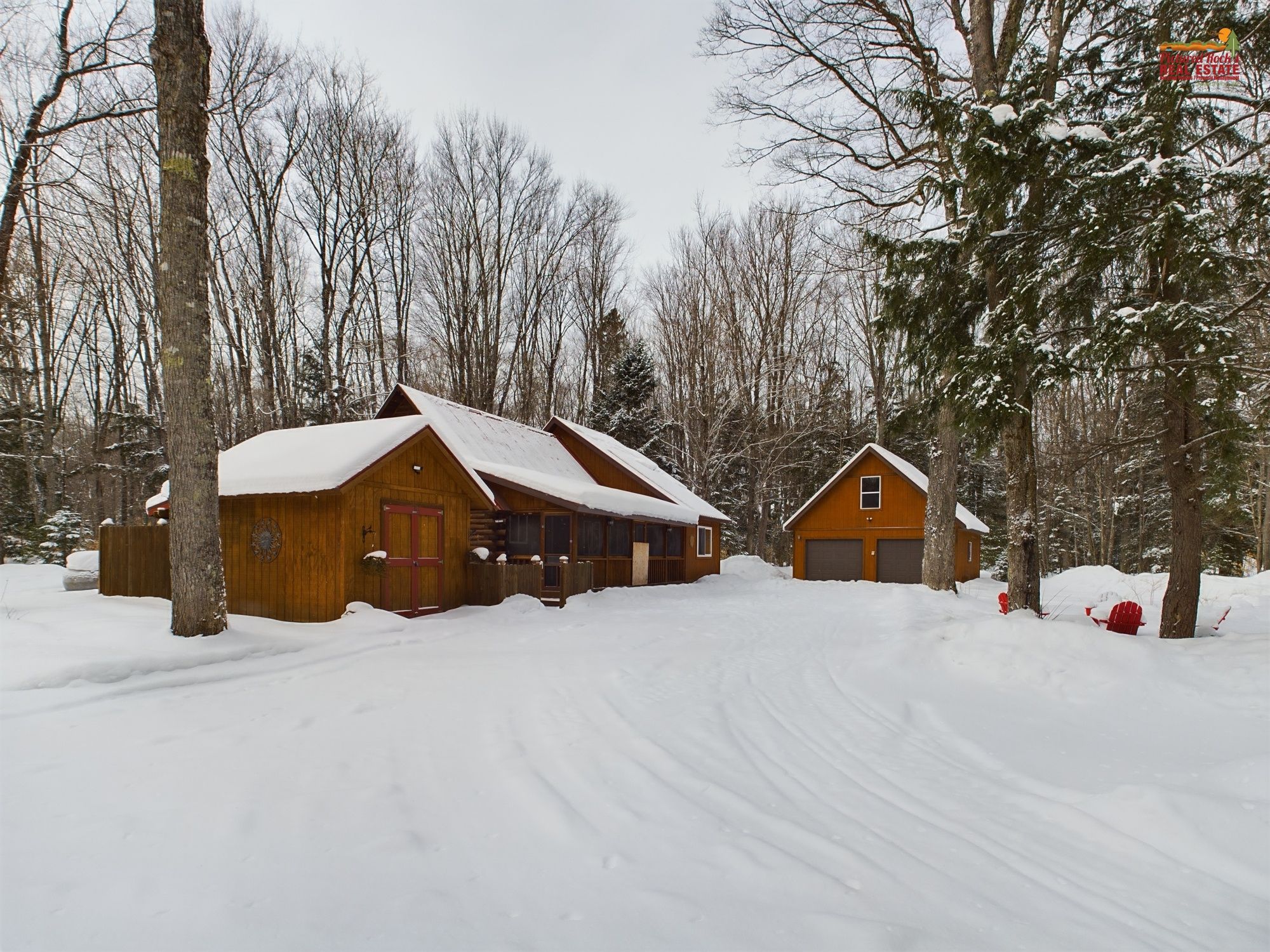 A cabin with a wooden exterior and a red door, surrounded by snow-covered trees and a clear sky.
