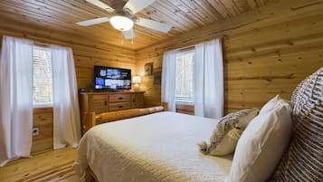A wooden cabin bedroom with a bed, a television, and a ceiling fan.