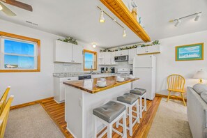 Cocina compacta con armarios blancos, una isla de madera y vistas al mar a través de las ventanas.