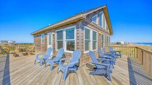 A wooden beach house with a deck, multiple windows, and several Adirondack chairs. - Semi-Oceanfront Dog Friendly Home w Newly Remodeled Kitchen, Grill, Beach Nearby (Waves)