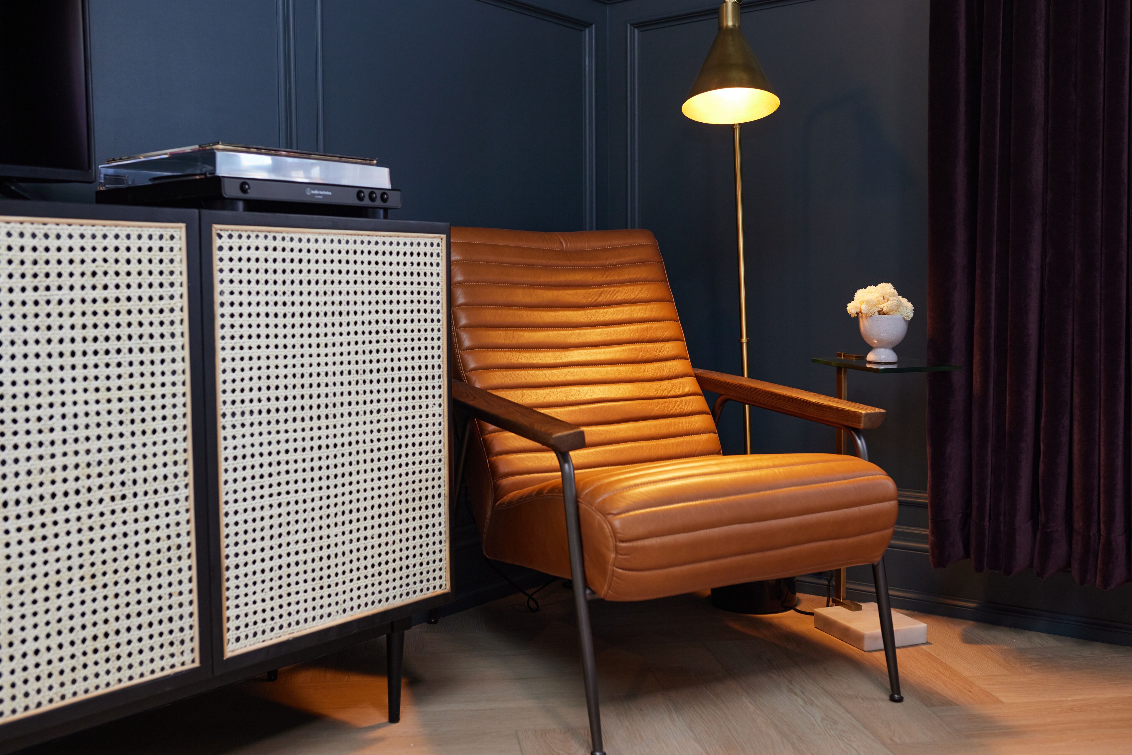 Una habitación moderna con un sillón de cuero, un mueble con diseño perforado y una lámpara de pie.