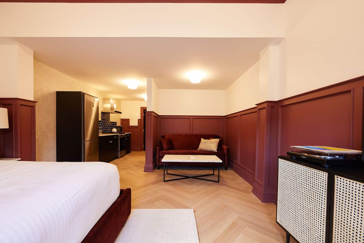 Ett hotellrum med en säng, en soffa, ett litet bord, ett litet kök och ett skåp.