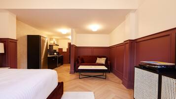 A hotel room with a bed, a sofa, a small table, a kitchenette, and a cabinet.