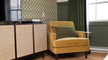 A room with a yellow armchair, a woven sideboard, and a patterned wallpaper.