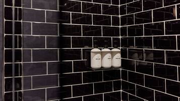 A bathroom with black tiled walls and three white bottles labeled "BODY WASH," "SHAMPOO," and "CONDITIONER" on a shelf.