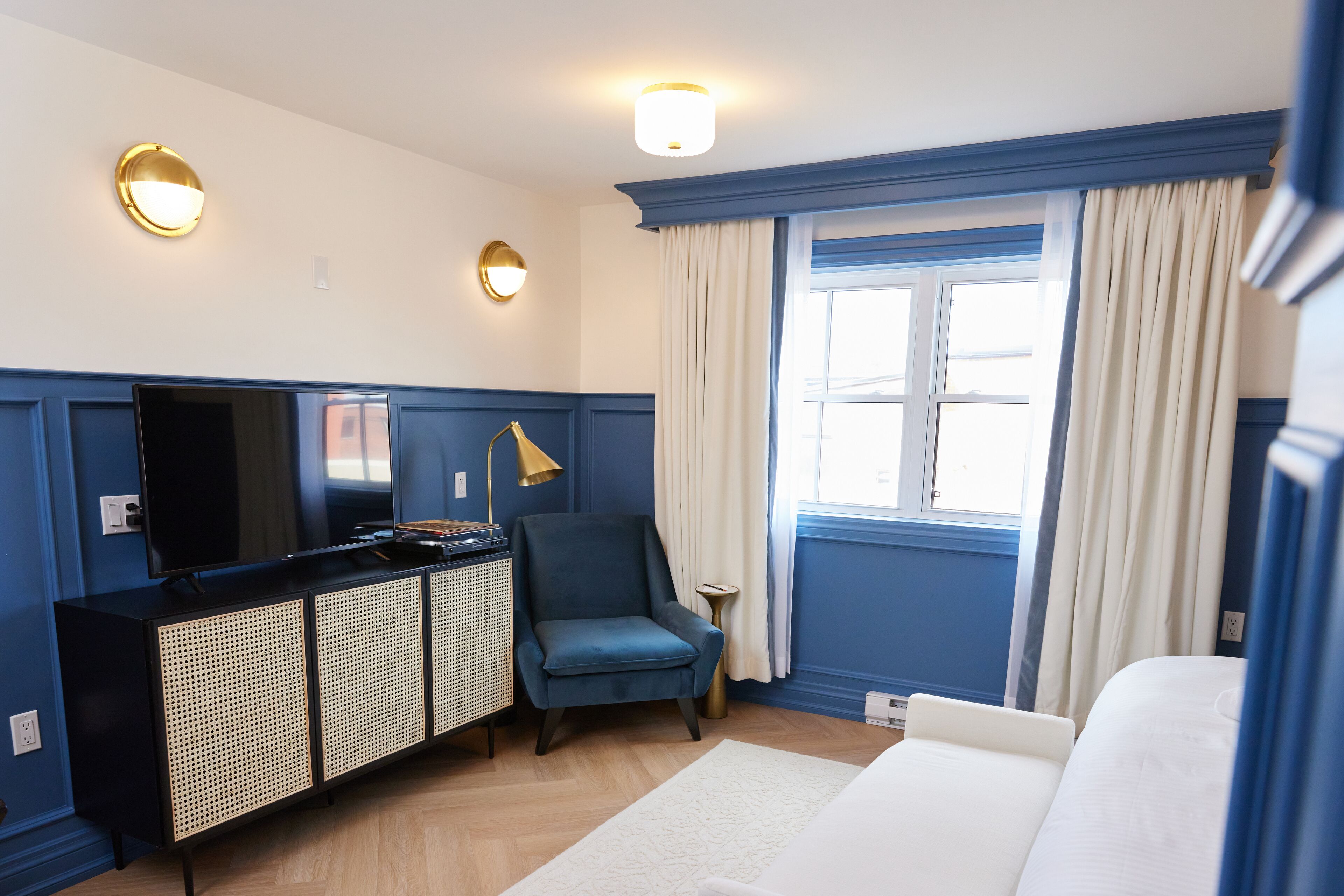 Una habitación de hotel con una cama, un escritorio con computadora, una silla, un televisor y una ventana con cortinas.