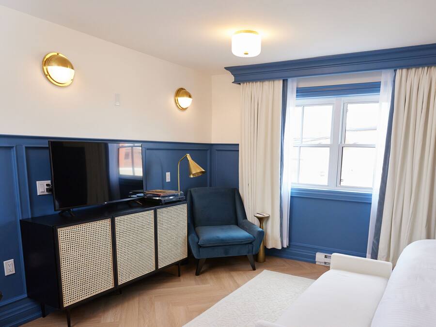 Una habitación de hotel con una cama, un escritorio con computadora, una silla, un televisor y una ventana con cortinas.