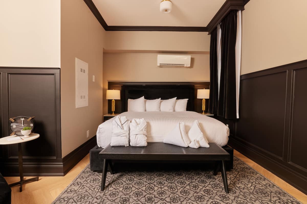 Ett hotellrum med en stor säng, sänglampor, ett litet bord med en klocka och en mönstrad matta.