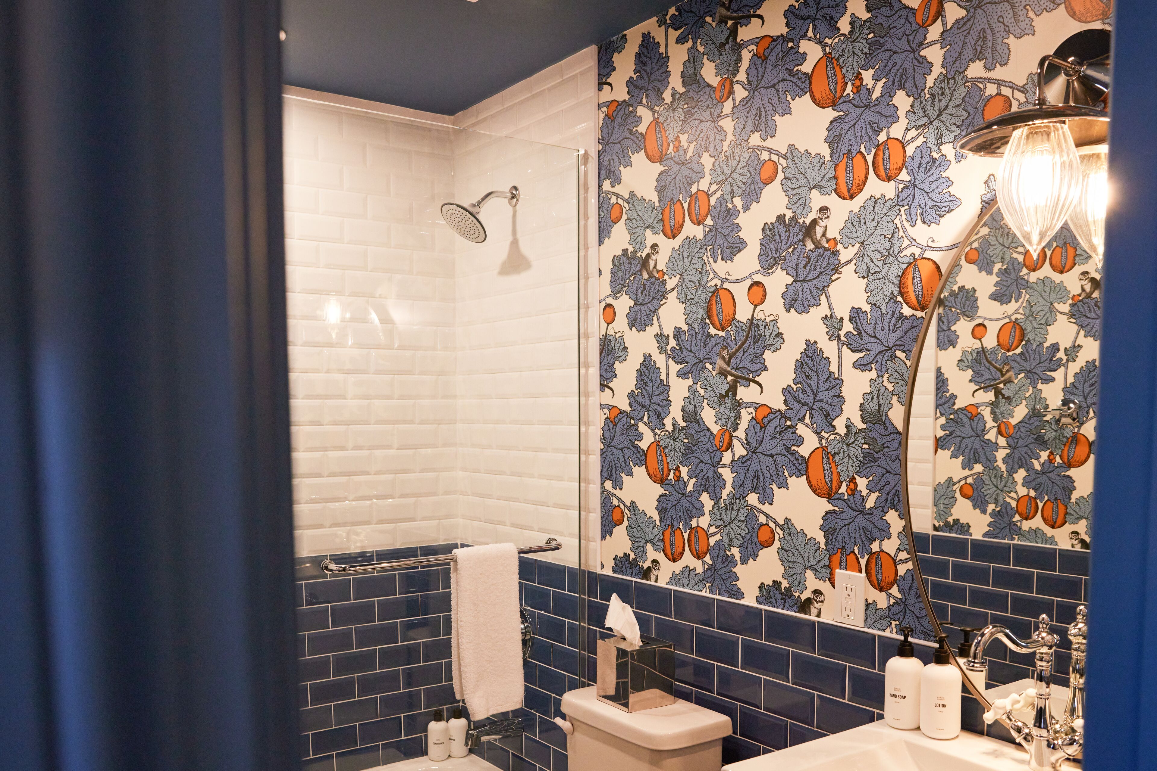 A bathroom with a white shower, a blue tiled wall, and a sink with toiletries.