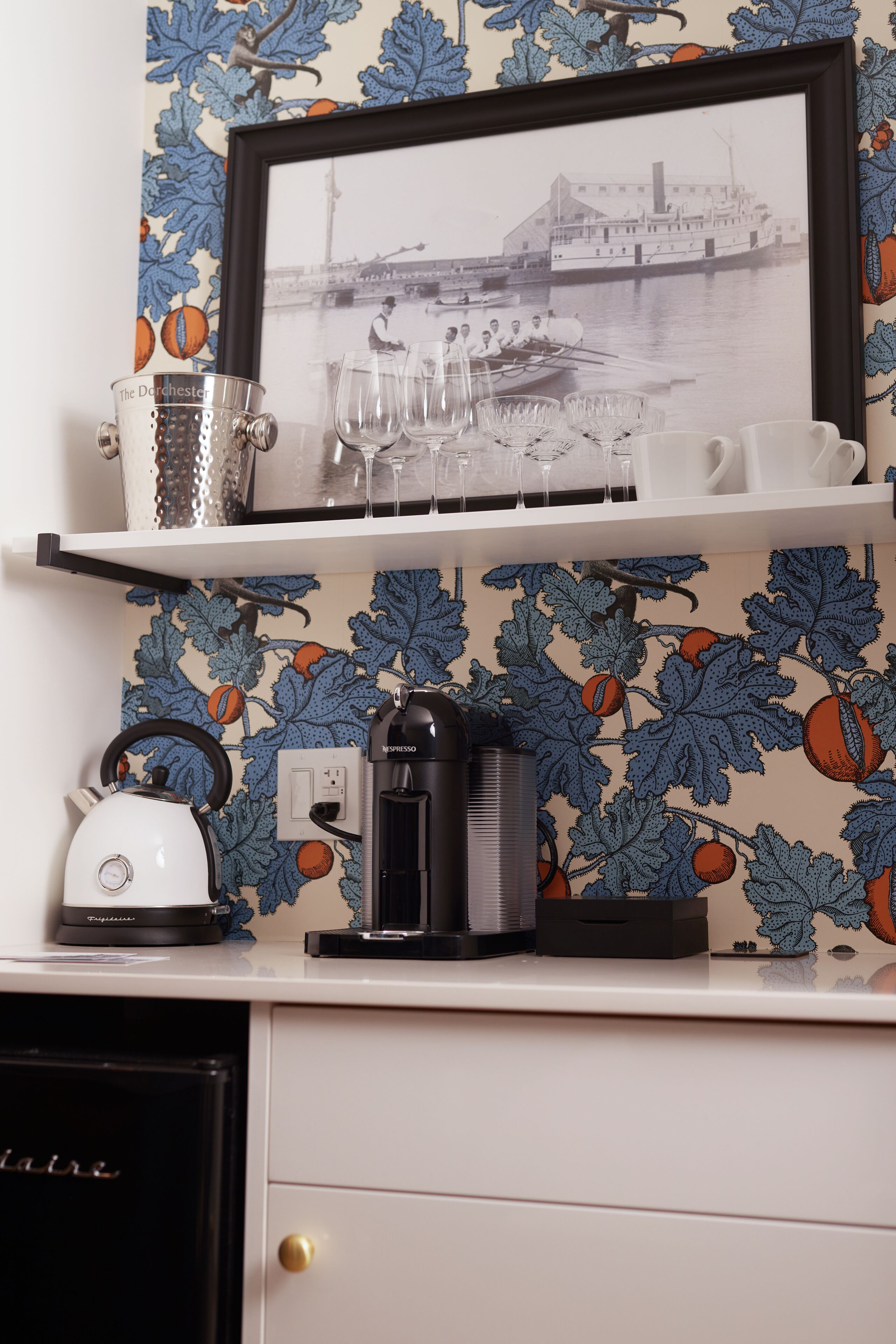 A kitchen counter with a coffee maker, kettle, and a framed picture above.