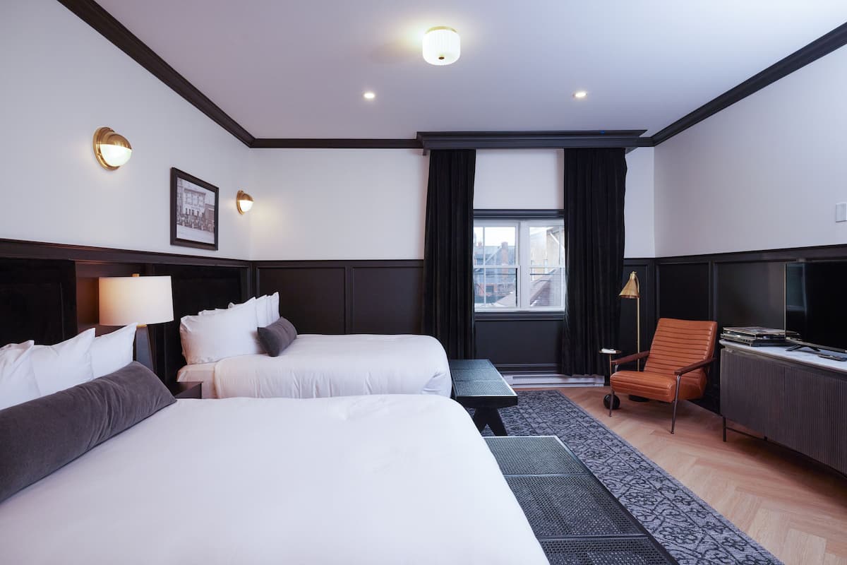 Ett hotellrum med två sängar, ett skrivbord, en stol, en tv och ett fönster med gardiner.