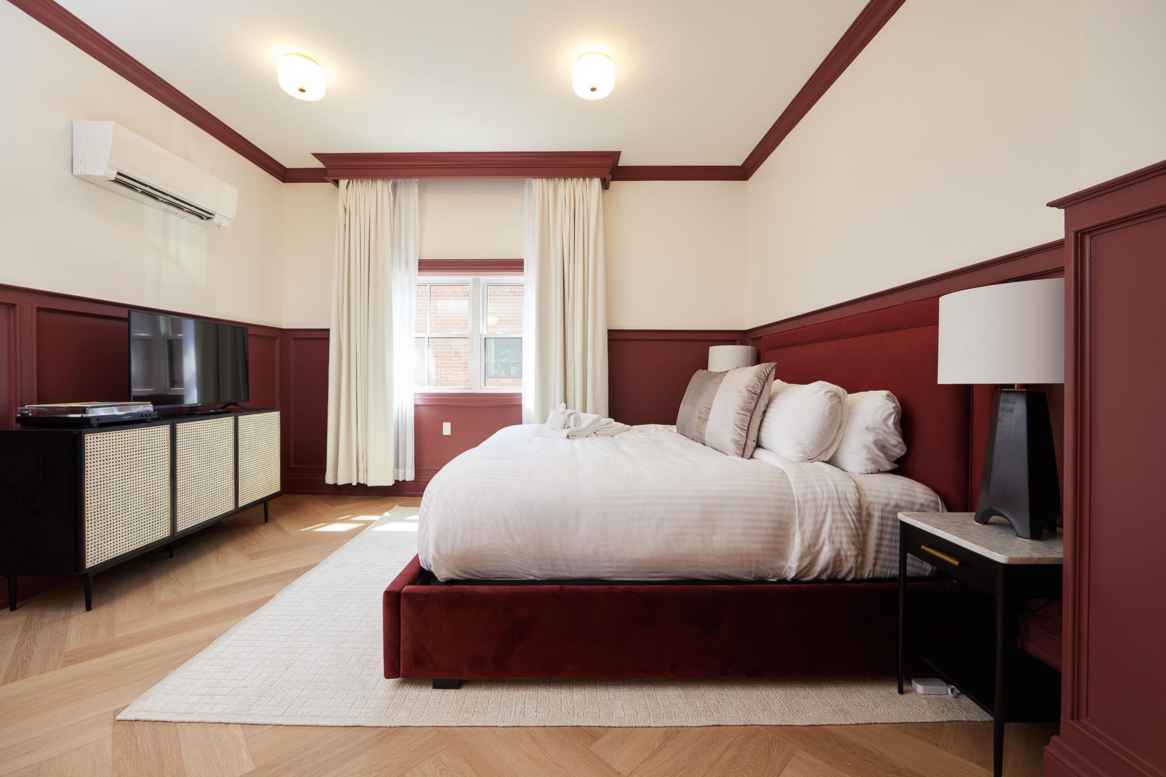 A bedroom with a large bed, a TV, a desk, and a window with curtains.