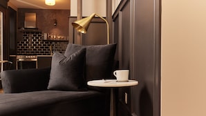 Una sala de estar moderna con un sofá negro, una mesita redonda con una taza blanca y una lámpara dorada.