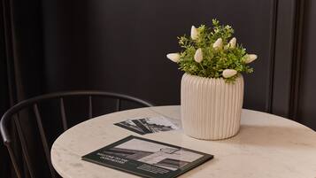 A round table with a white marble top, a white ribbed vase with green plants, and a black chair with metal legs.