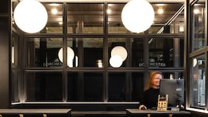Mostrador de recepción con diseño negro y dorado, techo de madera y felpudo negro con el nombre del hotel.