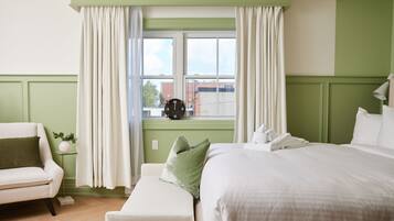 Une chambre d’hôtel avec un grand lit, un petit coin salon, une fenêtre avec des rideaux et une horloge au mur.