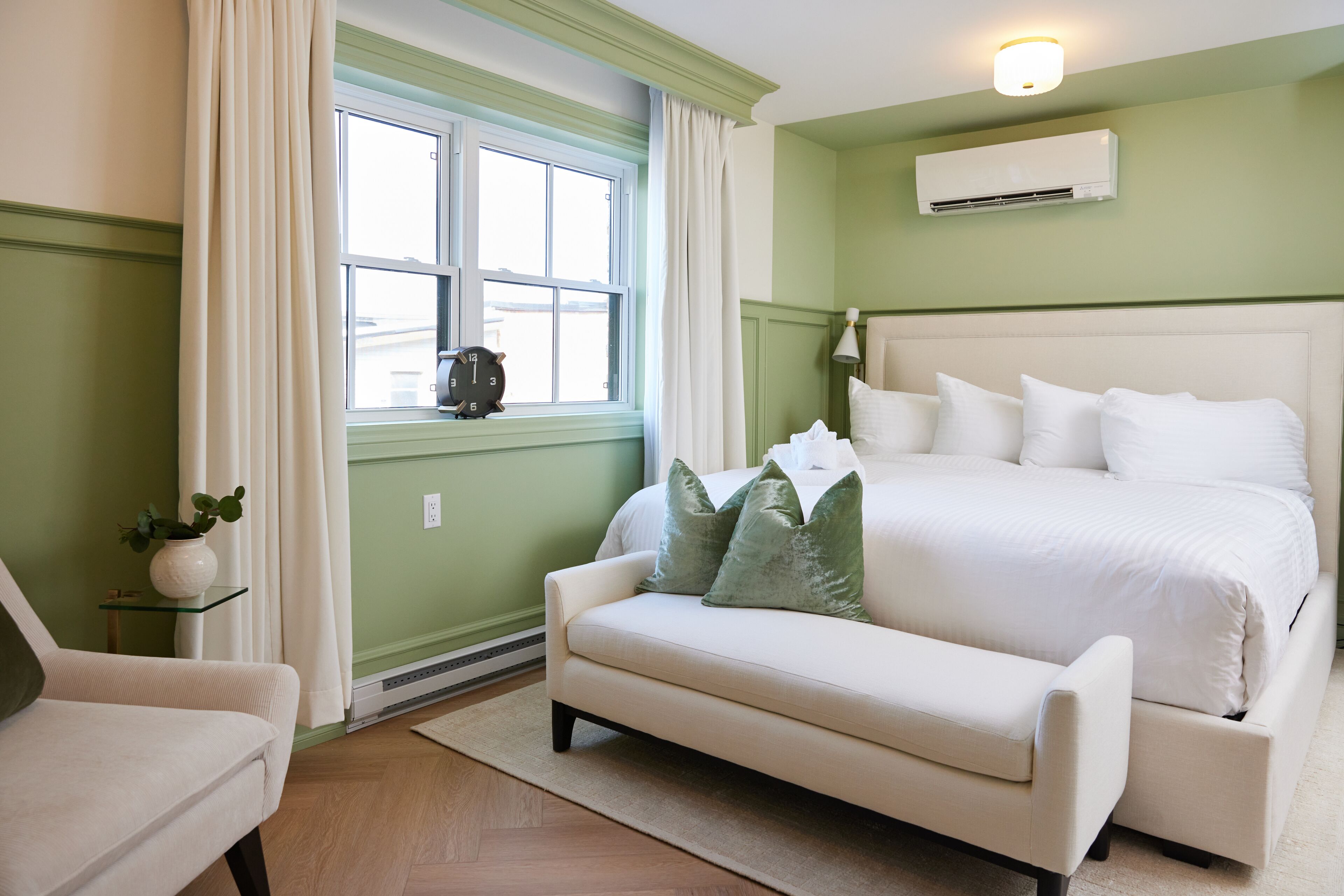 Un dormitorio con una cama grande, una mesita de noche con lámpara, una silla y una ventana con cortinas.