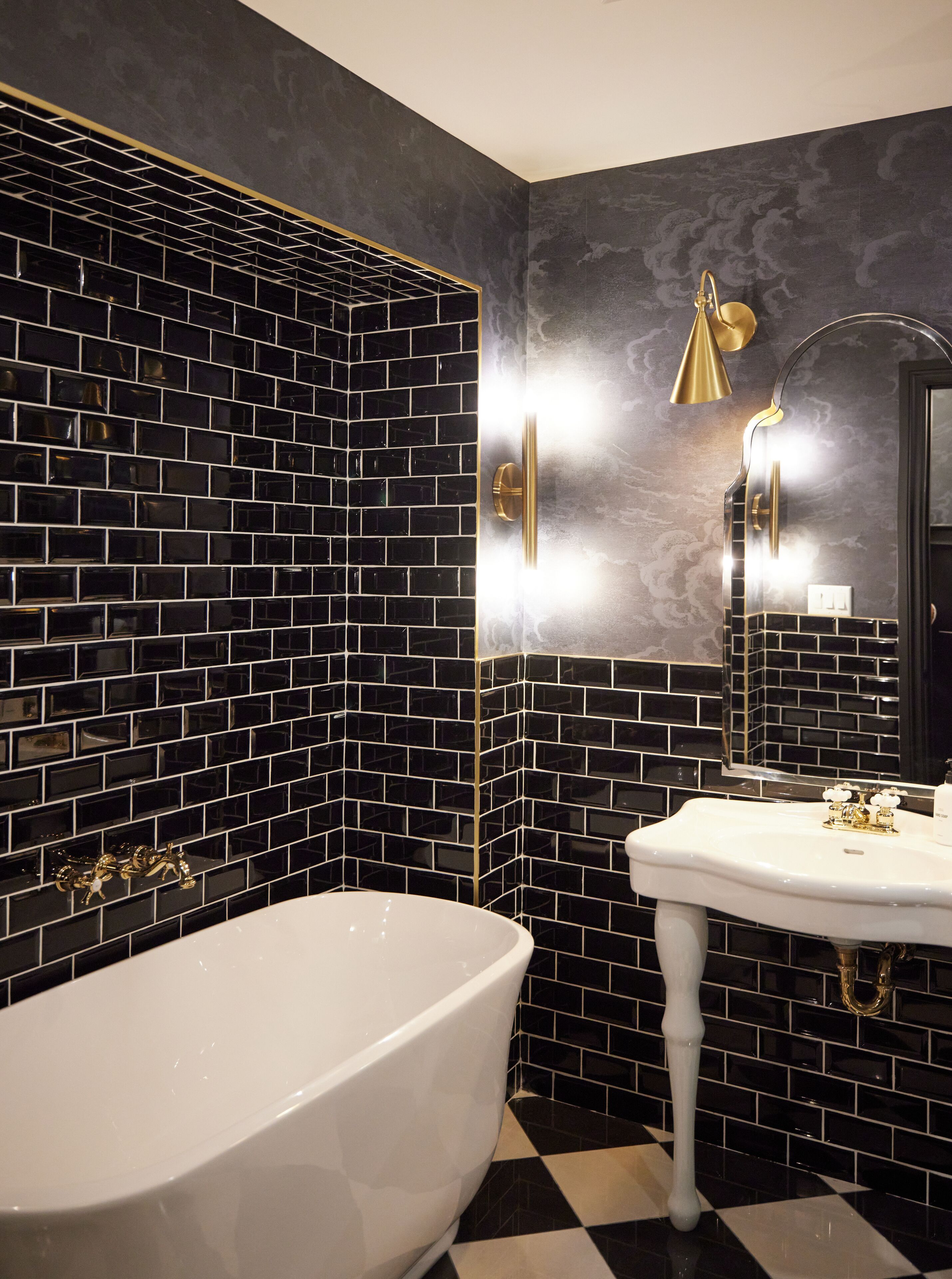 A bathroom with a black and white tiled wall, a white sink, and a gold-colored showerhead.