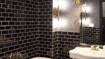 A bathroom with a black and white tiled wall, a white sink, and a gold-colored showerhead.