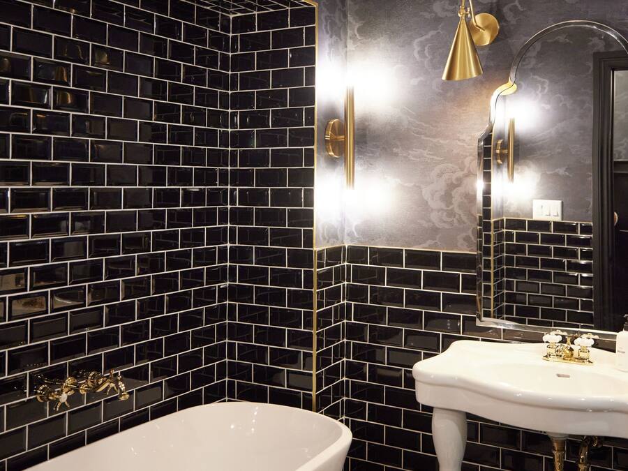 A bathroom with a black and white tiled wall, a white sink, and a gold-colored showerhead.
