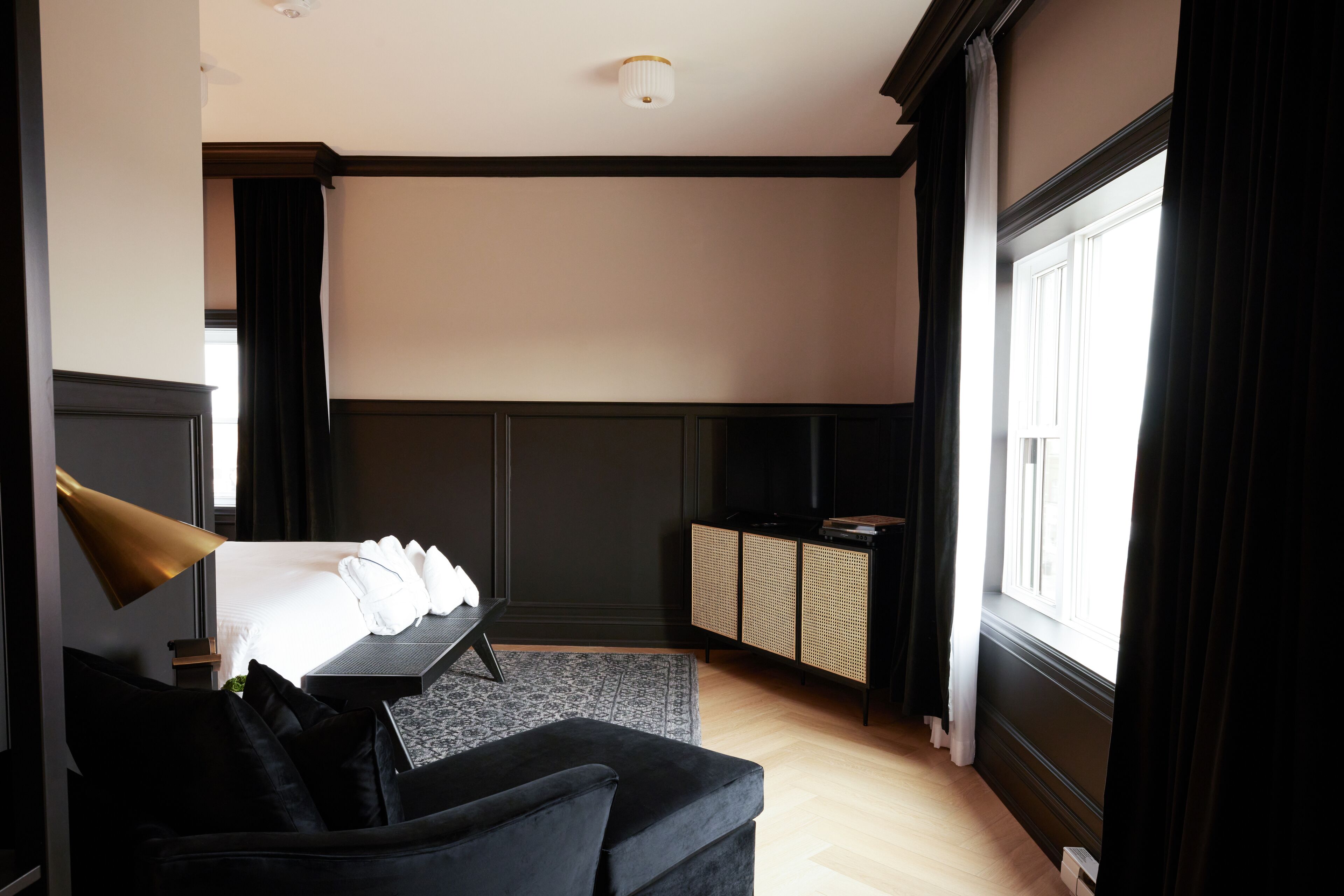 A hotel room with a bed, a black sofa, a desk, a television, and a window with curtains.