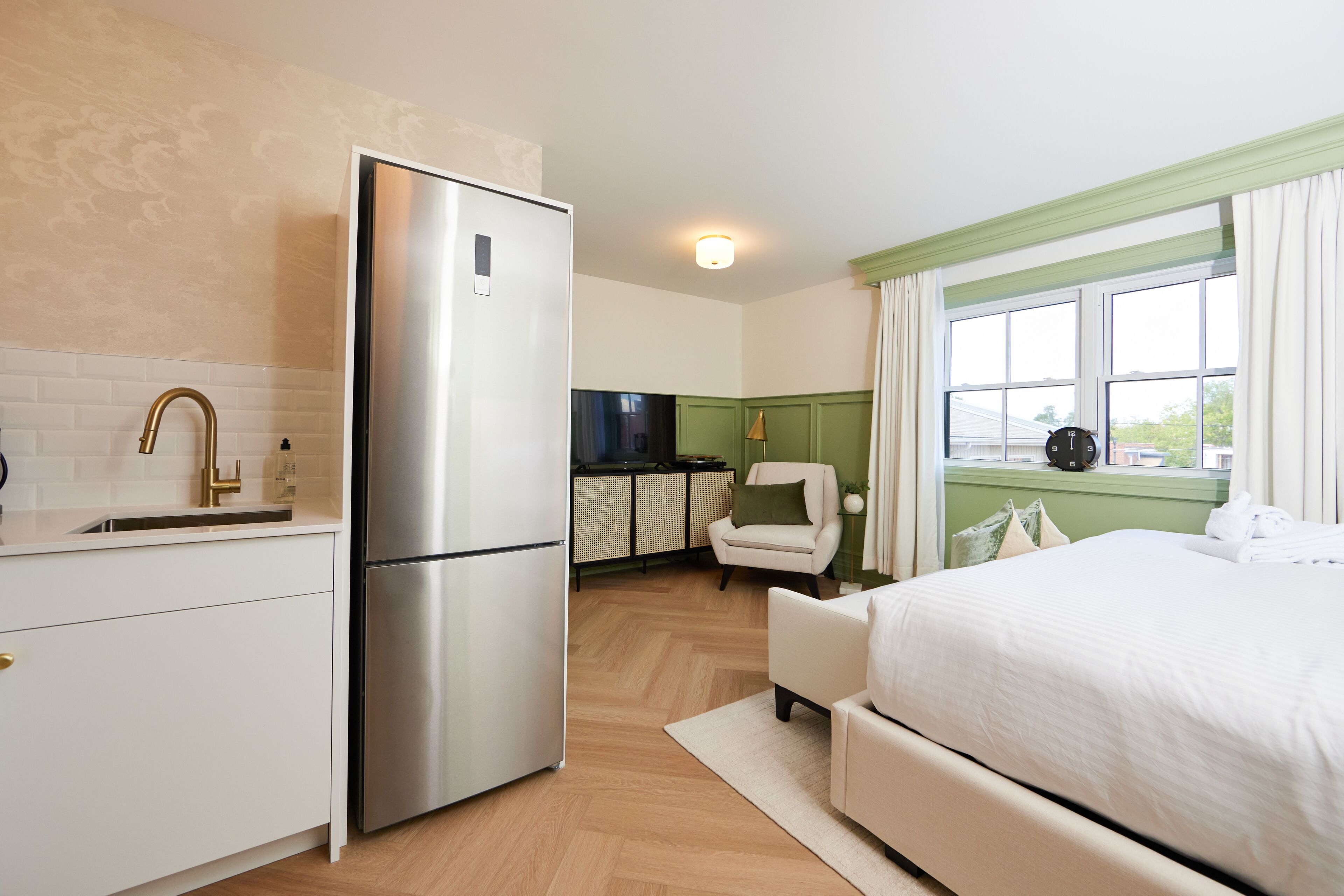 Una habitación de hotel compacta con kitchenette, cama, silla y ventana con cortinas.