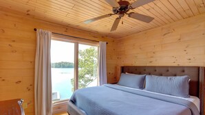 Een houten slaapkamer met een groot bed, een plafondventilator en een raam met gordijnen.