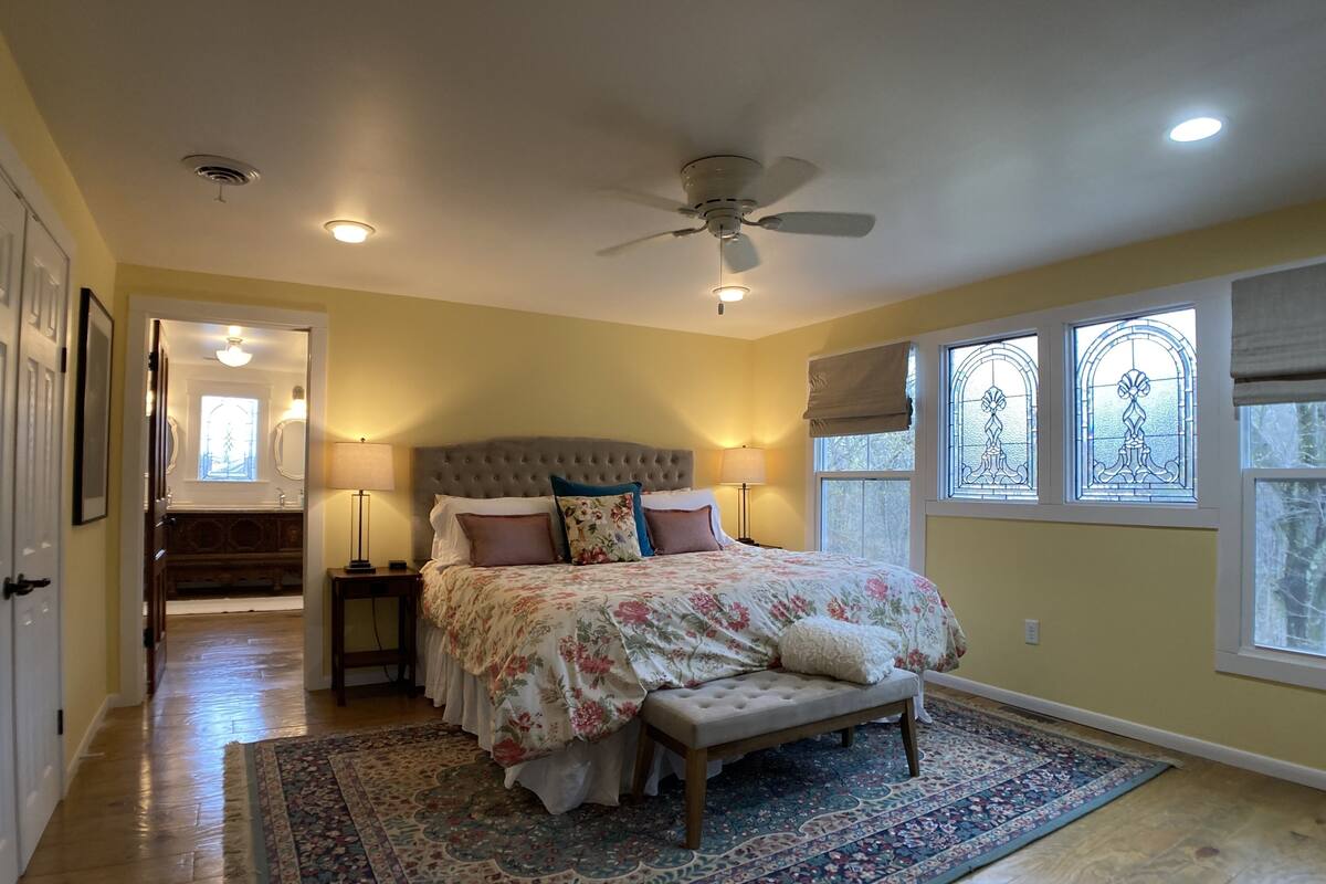 Une chambre avec un grand lit, un ventilateur de plafond et une vue sur l’extérieur par une fenêtre.