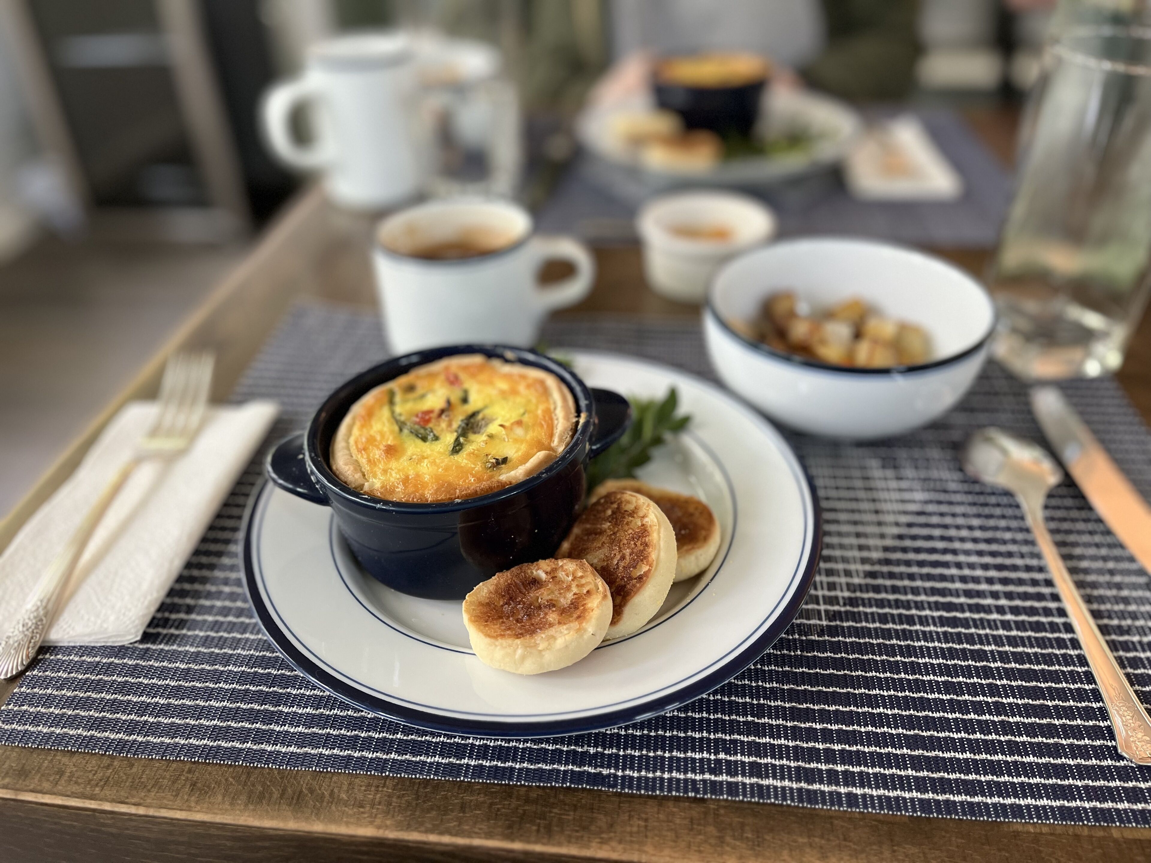 Un desayuno con una quiche, panqueques y café sobre una mesa.