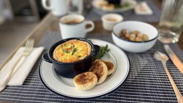 Un desayuno con una quiche, panqueques y café sobre una mesa.