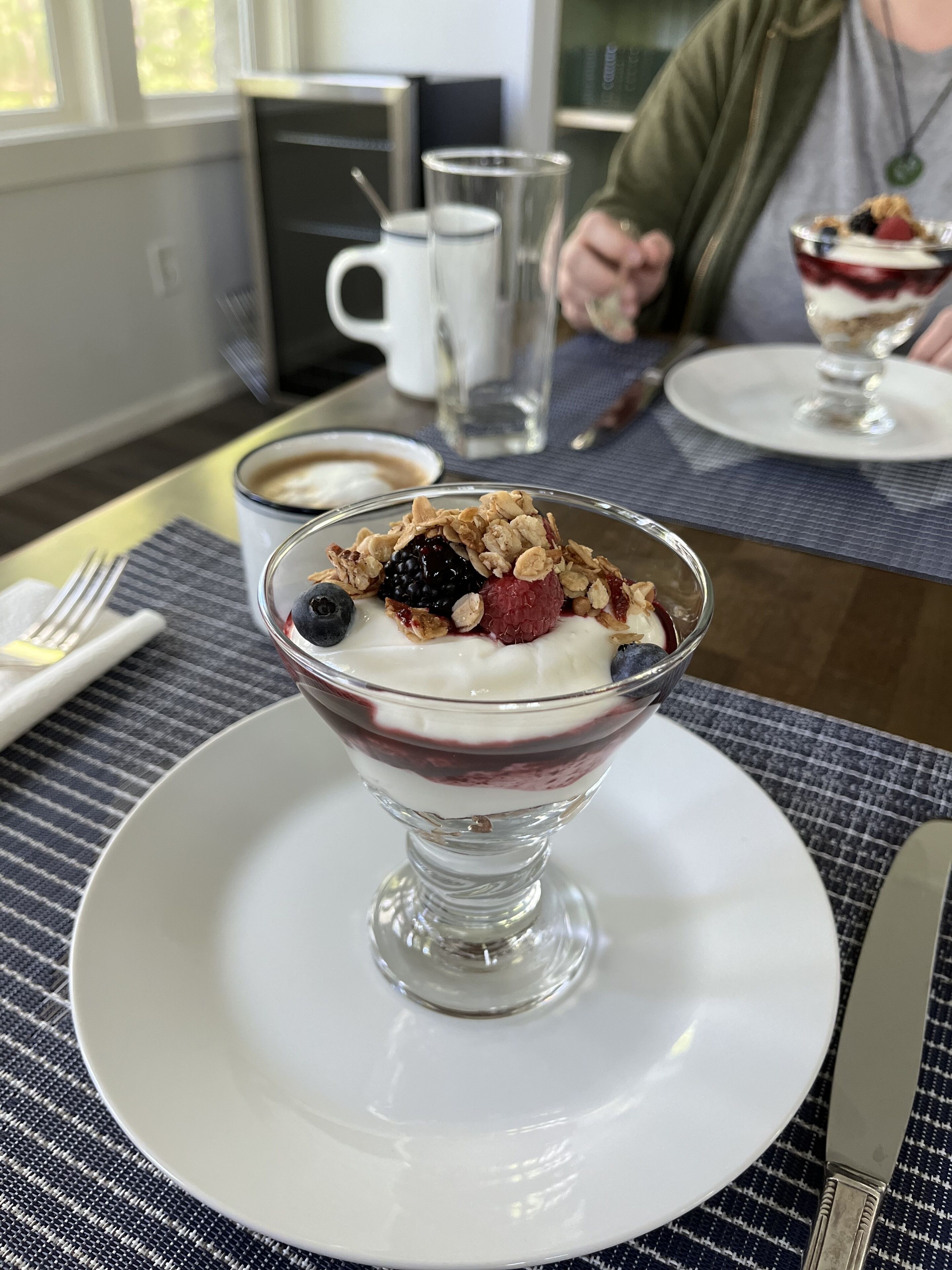 A dessert in a glass bowl on a white plate, with a fork and knife beside it.