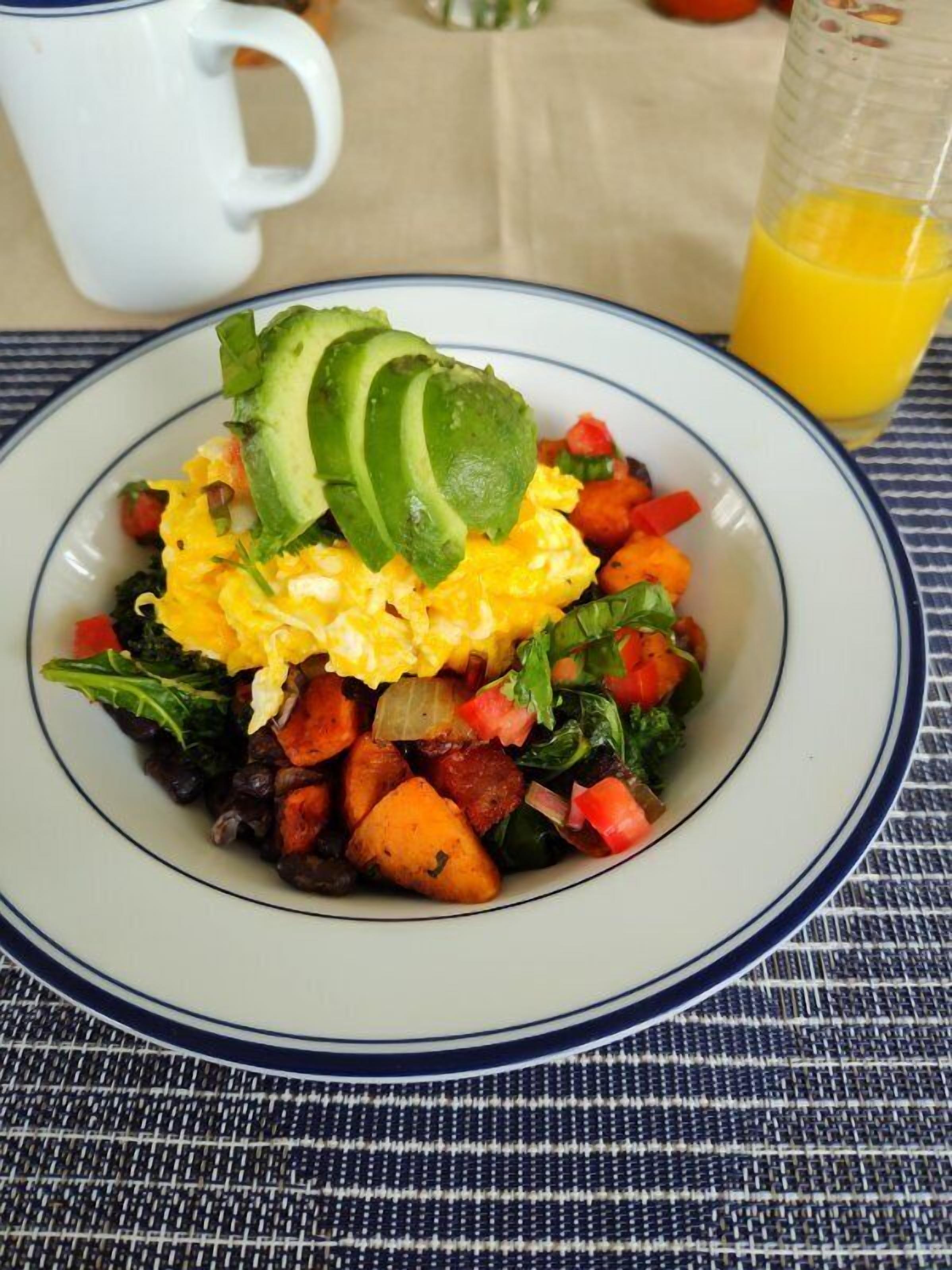 A plate of scrambled eggs, avocado slices, and mixed vegetables on a table with a striped tablecloth.