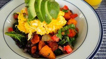 A plate of scrambled eggs, avocado slices, and mixed vegetables on a table with a striped tablecloth.