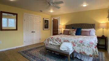 A bedroom with a large bed, a bench, a ceiling fan, and a nightstand with a lamp.