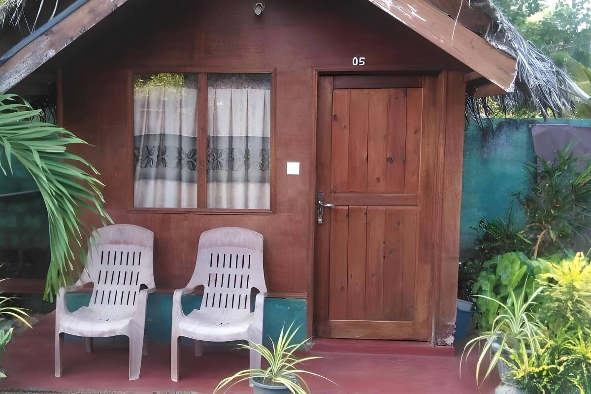 A small wooden house with a red door and two plastic chairs outside.