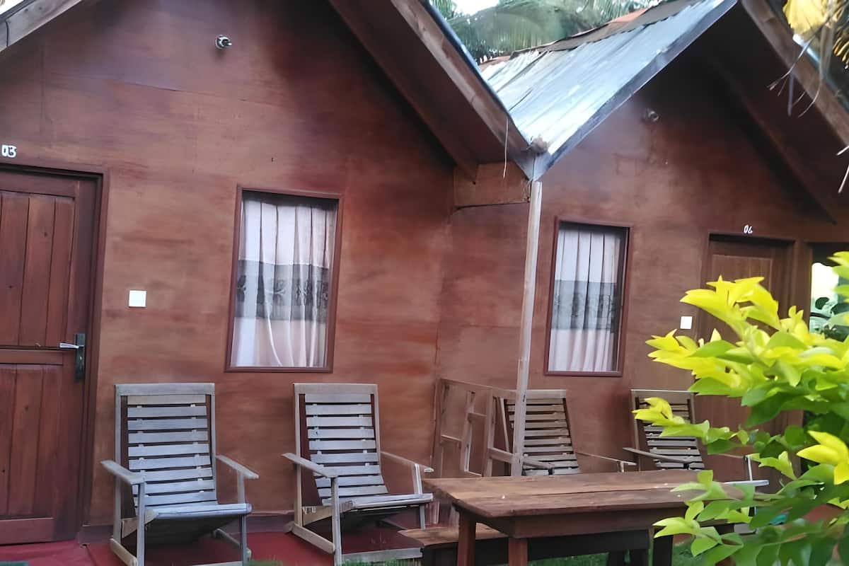 A rustic wooden cabin with two doors, two windows with curtains, and two wooden chairs and a table.