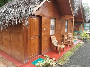 A wooden house with a thatched roof, a wooden door, and a small porch with two chairs. - Dolphin Bay Cabana Resort (Trincomalee)