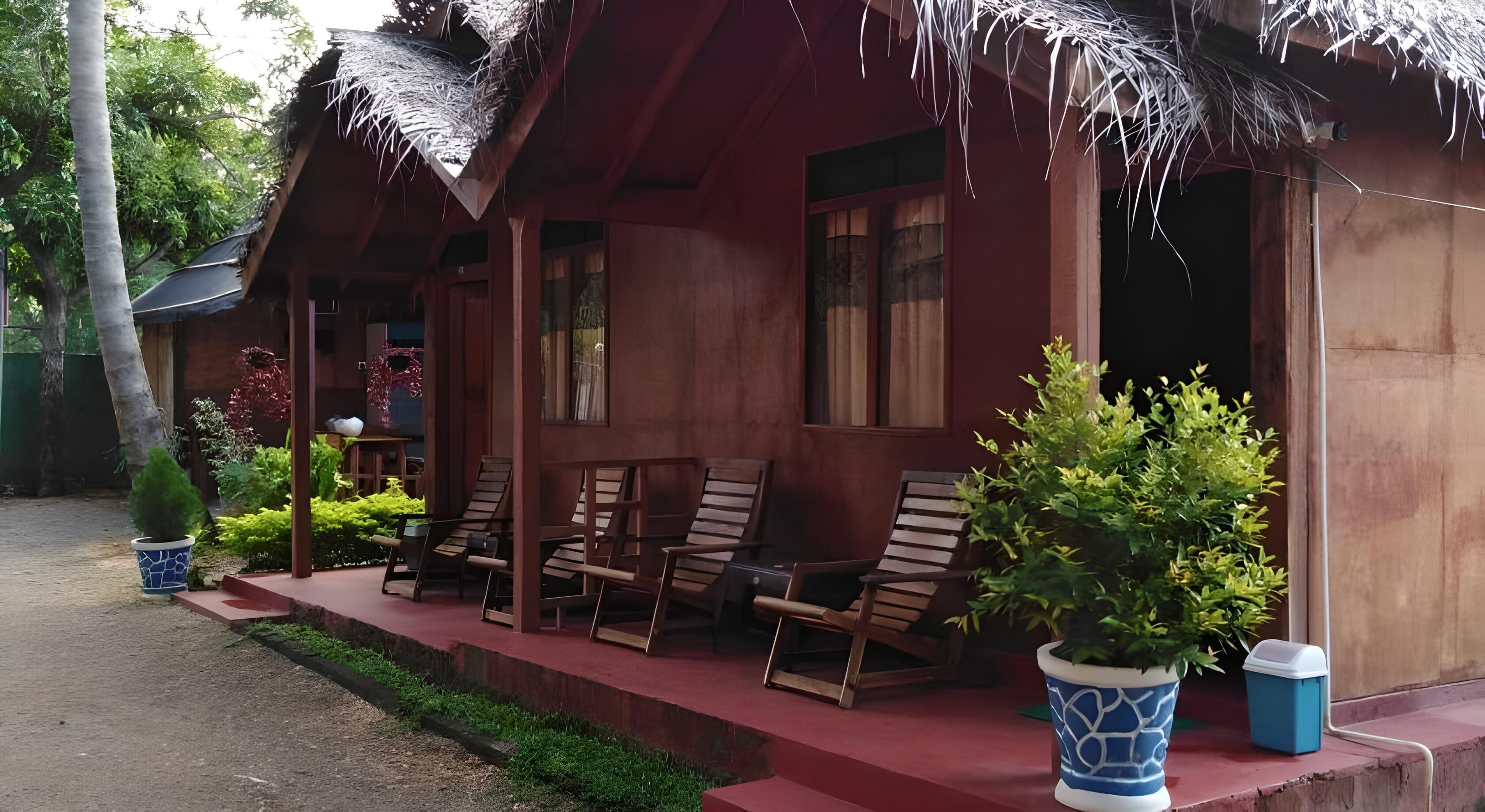 A wooden house with a thatched roof, a porch with wooden chairs, and potted plants.