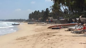 A beach with boats, palm trees, and beach chairs. - Dolphin Bay Cabana Resort (Trincomalee)