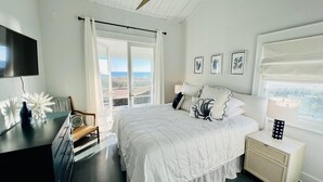 A bedroom with a bed, a desk, a chair, a nightstand, a lamp, and a ceiling fan. - "Beach Box" BHI and Shoals Club, Pet Friendly, Ocean Views, Steps To Beach (Bald Head Island)