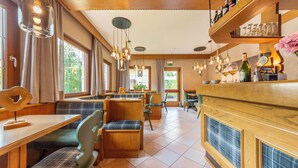 A restaurant with wooden furniture, hanging lights, and a bar area with bottles and glasses.